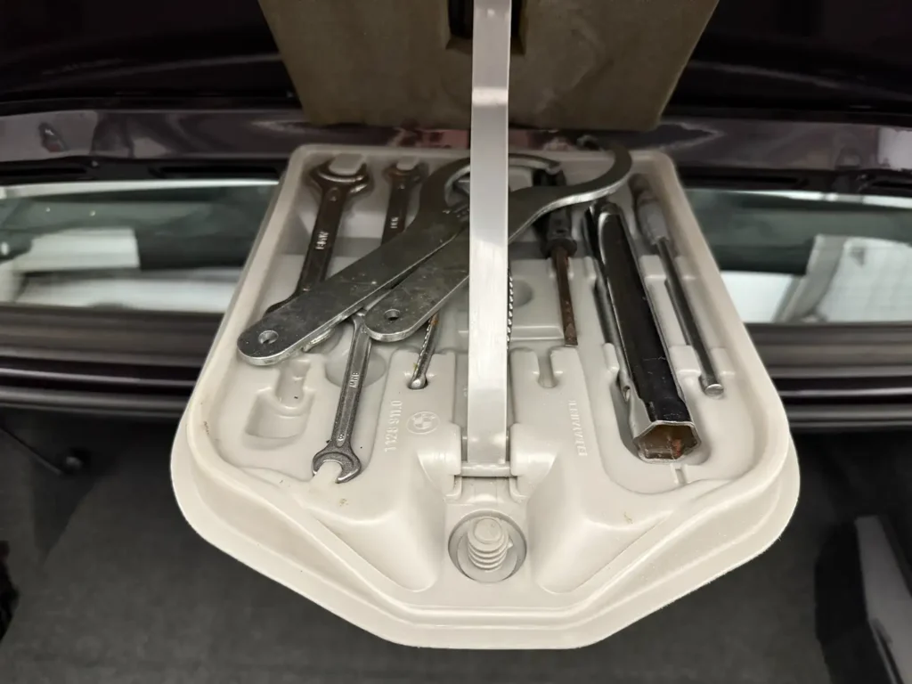 Bordwerkzeug eines BMW 325i E30 AC Schnitzer im Heritage-Stil, klassisches Zubehör im Kofferraum- oder Werkzeugset-Layout.