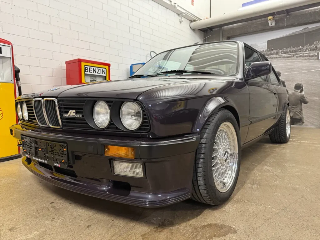 Frontansicht eines klassischen BMW 325i E30 mit AC Schnitzer Modifikationen, mit Fokus auf Stoßstange, Scheinwerfer und Vorderrad im zeittypischen Design