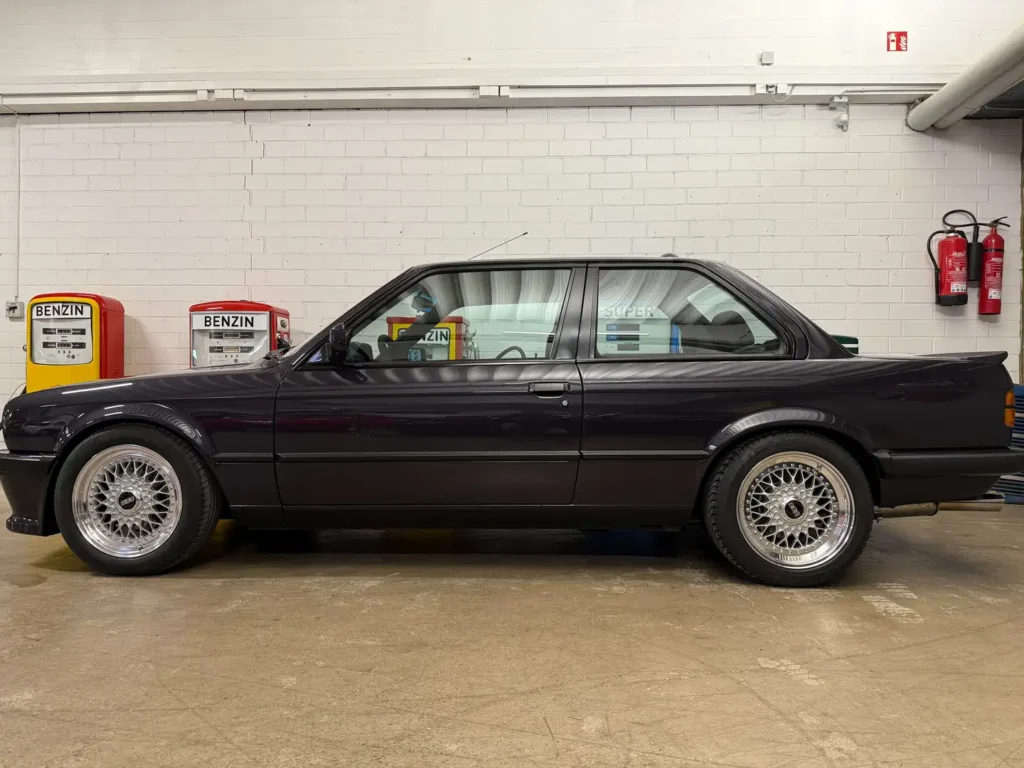 Seitenansicht eines BMW 325i E30 AC Schnitzer Coupé in Macaoblau, klassisches Design mit Fokus auf Karosserieform und Felgen