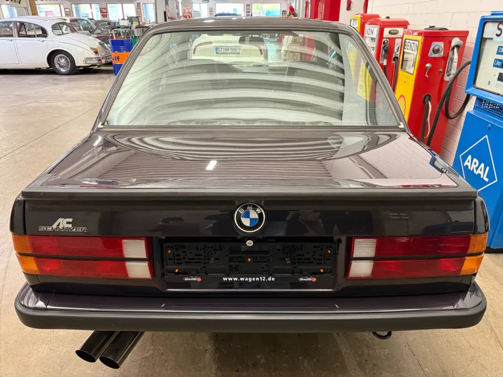 Heckansicht eines BMW 325i E30 AC Schnitzer Coupé in Macaoblau, klassisches Design mit sichtbarem Kofferraum und Abgasanlage (Auspuff) im Fokus