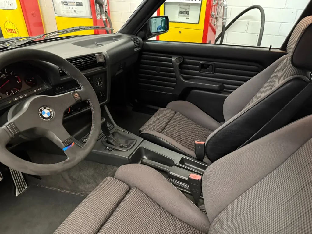 Cockpit eines BMW 325i E30 mit AC Schnitzer Ausstattung, Fahrerperspektive auf klassisches Armaturenbrett mit analogen Anzeigen, sportlichem Lenkrad und klar strukturierten Bedienelementen