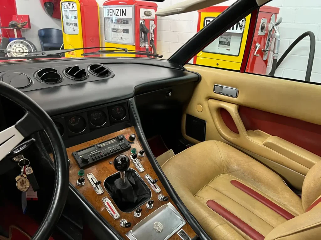 Innenraum eines seltenen, handgeschalteten Ferrari 400i mit Schaltkonsole, beigem Leder, roten Akzenten und klassischem Armaturenbrett mit analogen Instrumenten