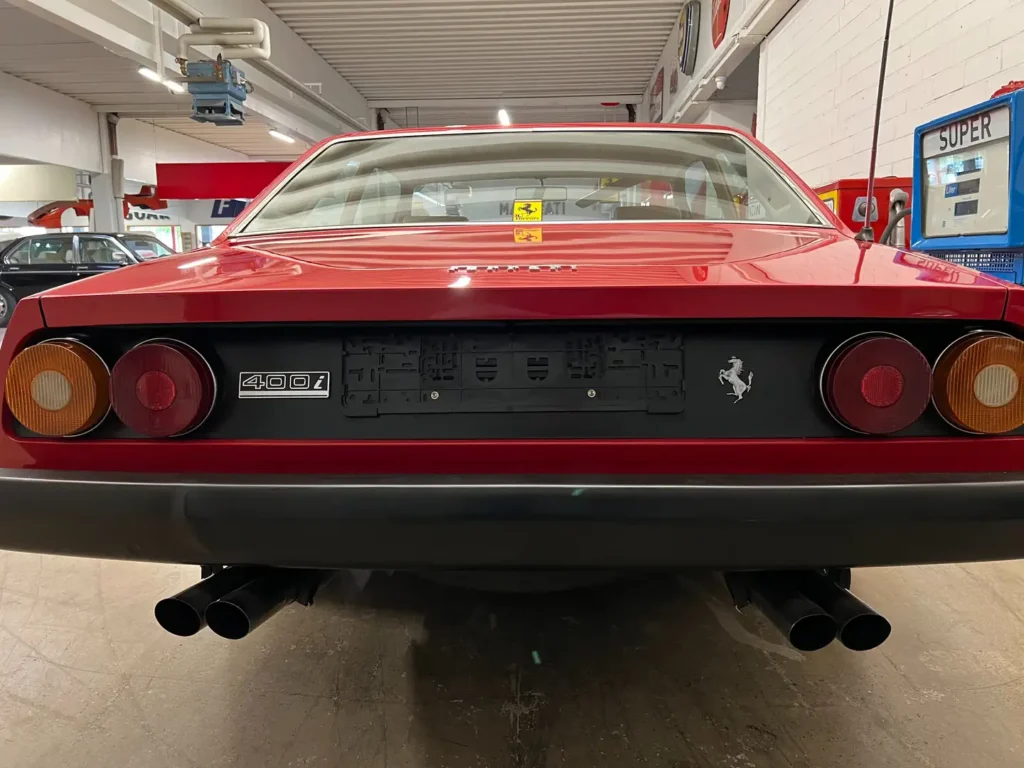 Heckansicht eines seltenen Ferrari 400i mit manueller Schaltung im klassischen Design, mit Fokus auf Auspuff, Ferrari-Emblem und Rücklichtern Vierrohr Auspuff.