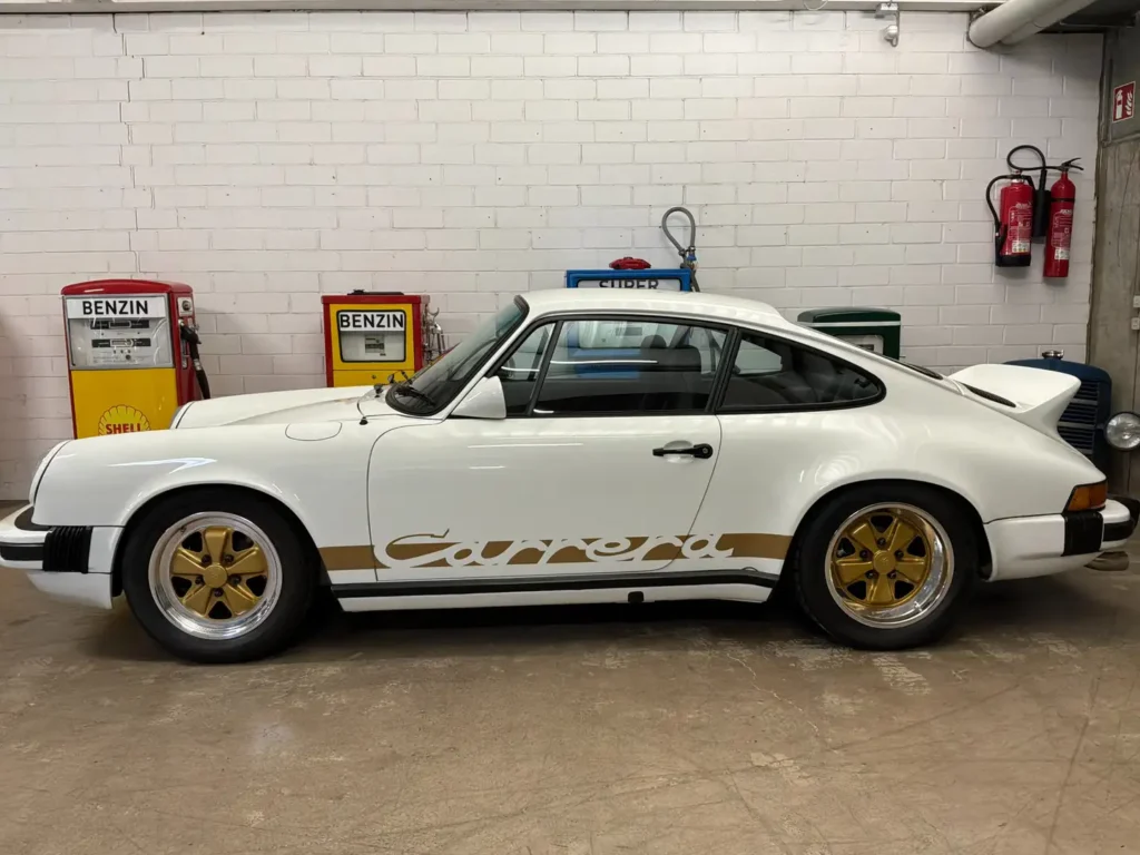 Porsche Carrera 1975 weisses Coupe Seitenansicht vor Zapfsaeulen.